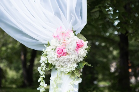 Beautiful white arch with flower decorations for the wedding ceremony with chairs for guests on the green background with treesの写真素材