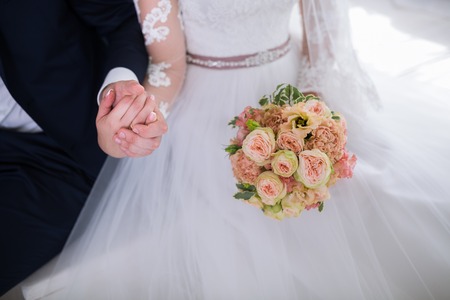 Wedding. Beautiful Weding bouquet of different flowers in the hands of the bride in a white wedding dress. Bride with a wedding bouquet holding grooms hand. Wedding ceremonyの写真素材