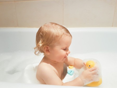 A little 1,5 year-old baby boy playing with toys in a bubble bath. Cute kid washing with foam in bathtubの写真素材