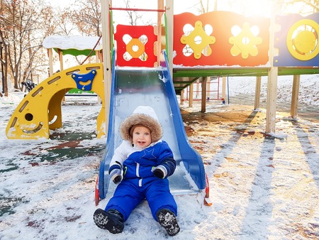 Happy kid playing on slide in the playground at sunny winter dayの写真素材