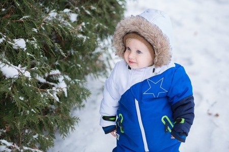 Year-old laughing baby boy in warm snowsuit walking in the winter park with a white snow. First winter and first toddler steps on the snowの写真素材