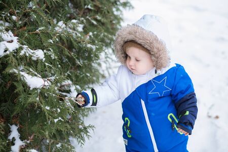 Year-old laughing baby boy in warm snowsuit walking in the winter park with a white snow. First winter and first toddler steps on the snowの写真素材