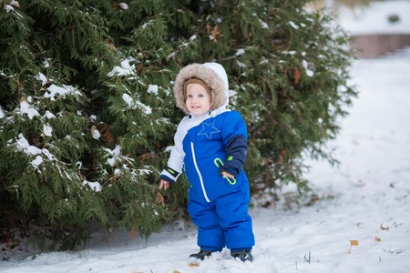 Year-old laughing baby boy in warm snowsuit walking in the winter park with a white snow. First winter and first toddler steps on the snowの写真素材