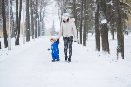 Mother and little toddler boy walking in the winter forest and having fun with snow. Family enjoying winter. Child and mom watching falling snow outdoors. Winter lifestyle concept.の写真素材