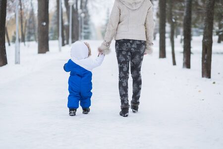Mother and little toddler boy walking in the winter forest and having fun with snow. Family enjoying winter. Child and mom watching falling snow outdoors. Winter lifestyle concept.の写真素材
