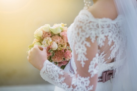 Wedding. Beautiful Weding bouquet of different flowers in the hands of the bride in a white wedding dress. Bride with a wedding bouquet on sunny day. Wedding sunshine conceptの写真素材