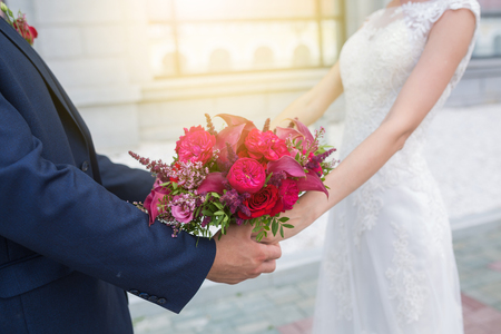 Wedding. Beautiful Weding bouquet of different flowers in the hands of the bride in a white wedding dress. Bride with a wedding bouquet holding grooms hand. Wedding ceremonyの写真素材