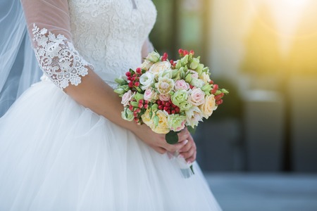 Wedding. Beautiful Weding bouquet of different flowers in the hands of the bride in a white wedding dress. Bride with a wedding bouquet on sunny day. Wedding sunshine conceptの写真素材