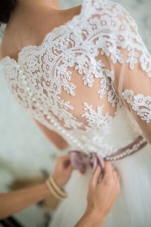 Wedding. Bridesmaid dresses bride for the wedding day. Bridesmaid helps bride with a wedding dress before the ceremony. Luxury bridal dress close up. Best wedding morning. Wedding conceptの写真素材