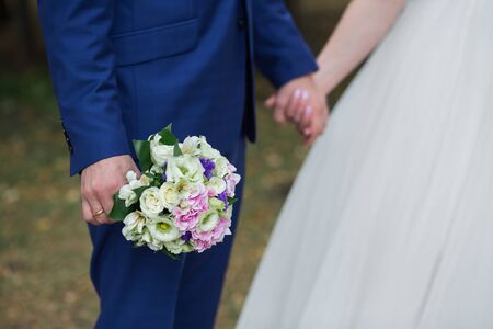Beautiful Weding bouquet of different flowers in the hands of the bride in a white wedding dress. Bride holding grooms hand. Wedding ceremony conceptの写真素材