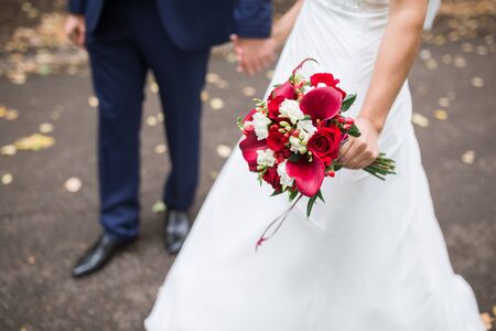 Beautiful Weding bouquet of different flowers in the hands of the bride in a white wedding dress. Bride holding grooms hand. Wedding ceremony conceptの写真素材