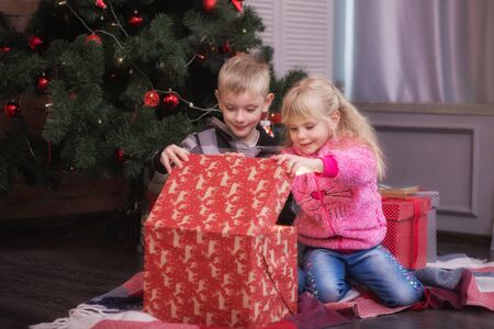 Family on Christmas eve in living room. Kids opening Xmas presents. Children under Christmas tree with gift boxes. Decorated room with traditional Christmas tree. New years warm winter evening at homeの写真素材