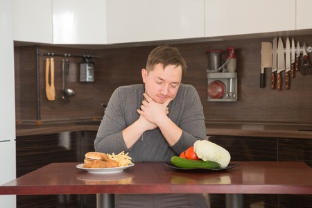 Man chooses between fast food and vegetables in the kitchen. Harmful - burger and fries unhealthy and wholesome food, lifestyle concept.の写真素材