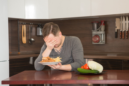 Man chooses between fast food and vegetables in the kitchen. Harmful - burger and fries unhealthy and wholesome food, lifestyle concept.の写真素材