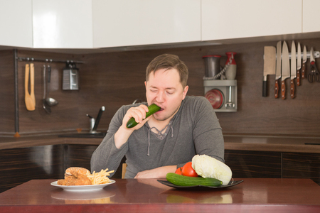 Man chooses between fast food and vegetables in the kitchen. Harmful - burger and fries unhealthy and wholesome food, lifestyle concept.の写真素材