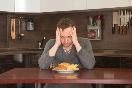 Fat man rejecting to eat junk food at home in the kitchen. Unhealthy food concept.の写真素材