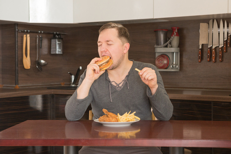 Young man eat junk food at home in the kitchen with pleasureの写真素材