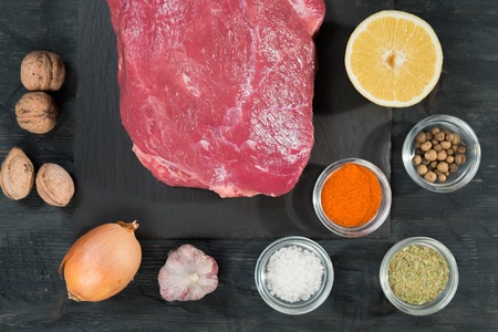Top view of raw meat. View from above of raw veal or beef steak on a slate black cutting board with spices and lemon.の写真素材