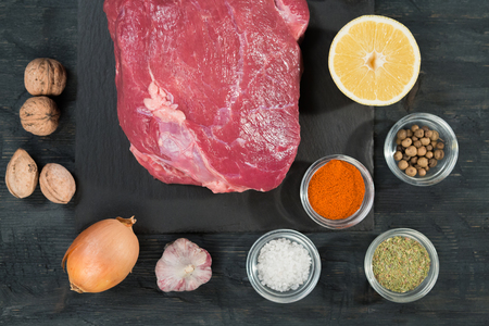 Top view of raw meat. View from above of raw veal or beef steak on a slate black cutting board with spices and lemon.の写真素材
