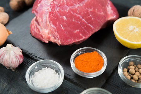 Close up of raw meat. Raw beef or veal steak on a slate black cutting board with spices and lemon.の写真素材