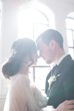 Sensual portrait of a young couple in Wedding day indoors near a big windowの写真素材