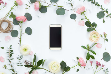 Flower arrangement on a white background with a mobile phone in a floral frame, top view and flat...