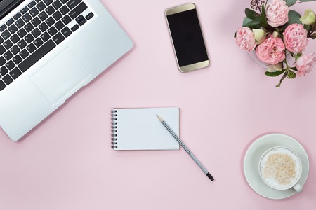 Top view of pink office desk table with laptop, smartphone, cup of coffee and flowers. Copy space, flat lay.の写真素材
