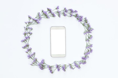 Flower arrangement on a white background with a mobile phone with white screen in a floral frame, top view and flat layの写真素材