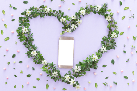 Top view of flower heart frame made of wildflowers, buds and leaves on lilac background. Love concept, flat lay.の写真素材
