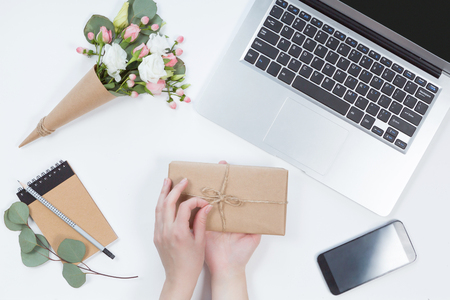 Top view of workspace with laptop, woman hands with present box, notebook, mobile phone on white background, flat layの写真素材