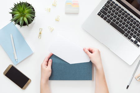Top view of woman hands opening envelope on white office table desk, flat lay. View from above of different chancellery stuff, layoutの写真素材