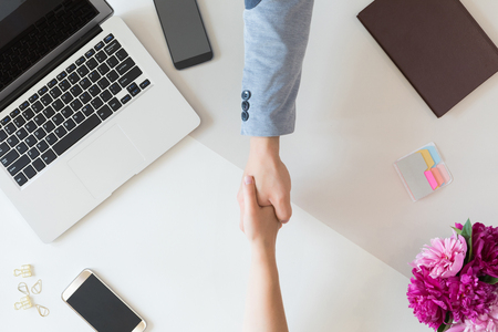 Top view of business team man and woman meeting and handshake concept, flat lay of office desk with laptop, notebook, mobile phone and flowersの写真素材
