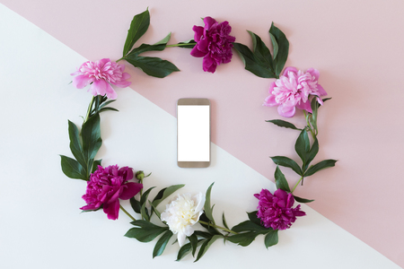 Flower arrangement on a white background with a mobile phone in a floral frame, top view and flat layの写真素材