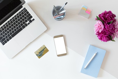 Top view of fashion office desk with credit card for online payment on laptop computer or mobile phone, flat lay on white background with cell phone and flowersの写真素材