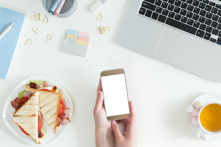Top view of break time on white office table desk. Business lunch in office, top view of sandwich, cup of green tea on white desk with laptop, mobile phone and notepad, flat lay.の写真素材