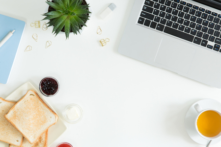 Overhead view of laptop, fresh sandwich, cup of green tea and mobile phone on white desktop table. Woman business and breakfast concept, top view and flat layの写真素材