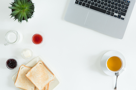 Overhead view of laptop, fresh sandwich, cup of green tea and mobile phone on white desktop table. Woman business and breakfast concept, top view and flat layの写真素材