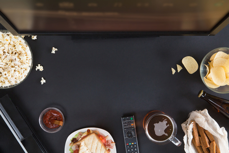 Top view of gamer accessorises and snacks frame, flat lay on black background with copyspace. Joystick and gamepad, keyboard, game console, mouse, mobile phone, beer, chips and popcorn.の写真素材