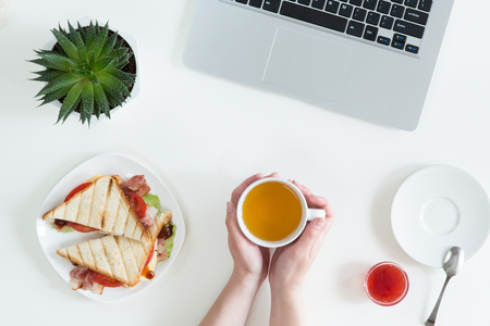 Top view of tasty and healthy business lunch in office, toast with jam, cup of tea on white office desk near laptop computer. Snack and food at break time, overhead view and flat layの写真素材