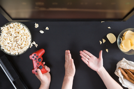 Man and woman playing video games together, top view of gamer accessorises and snacks frame, flat lay on black background. Joystick and gamepad, keyboard, game console, beer, chips and popcorn.の写真素材