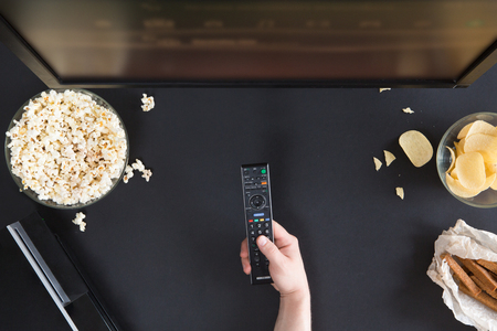 Popcorn, snack and a remote control for the TV, top view and flat lay on black backgroundの写真素材