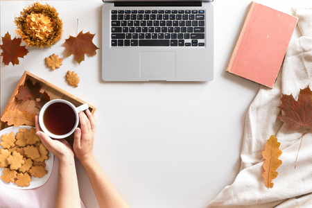Hello Autumn flat lay background. Top view of workspace or office desk with laptop, tea or coffee cup, maple leaves, vintage book and honey biscuits and cookies. lish office desk.の写真素材