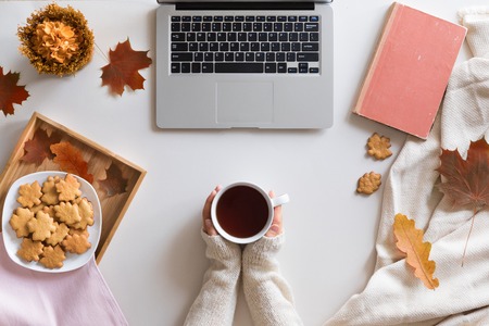 Top view and flat lay of autumn composition background. Laptop, cup of hot tea, book, autumn leaves and flowers, cinnamon cookies on white background.の写真素材