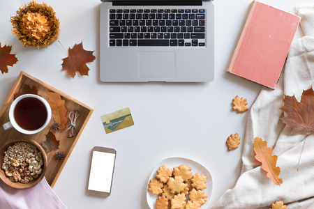 Top view of woman hands holding credit card on autumn baclground, business concept, online shopping, workspace with laptop, mobile phone, autumn leaves and flowers and notebook, cookies, flat lay.の写真素材