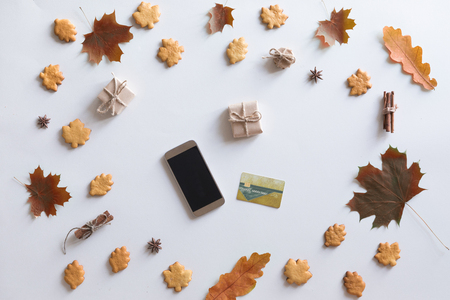 View from above of autumn background with mobile phone, credit card, autumn leaves, cookies, vintage book on white workspace. Top view and flat layの写真素材