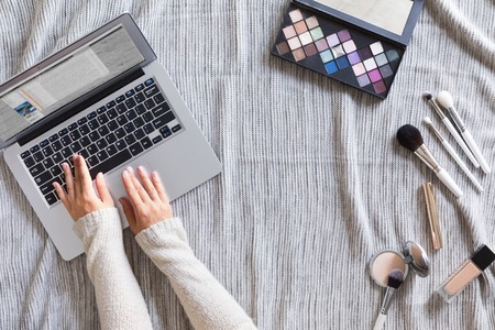 Cozy office table desk with computer laptop, autumn maple leaves, flowers, clipboard and beauty accessories, top view and flat lay. Home fashion women office workspace on knitted background.の写真素材