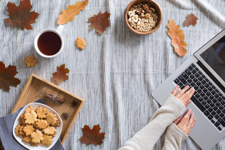 Flat lay and top view of home office desk. Workspace with woman hands, laptop, autumn leaves and flowers, cookies, coffee on cozy backgroundの写真素材