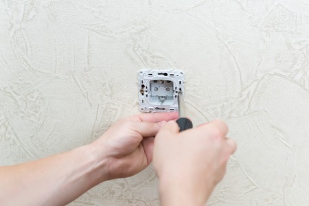 Male electrician puts on and repair an electrical outletの写真素材