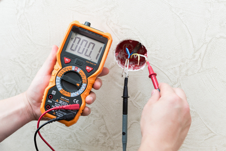Close-up of man measuring and cheking power supply voltage with digital multimeterの写真素材