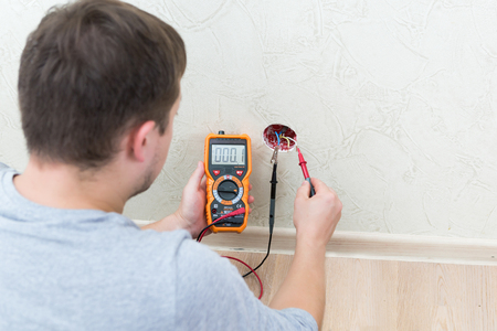 Close-up of man measuring and cheking power supply voltage with digital multimeterの写真素材